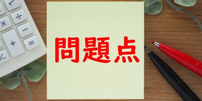 黄色の付箋に赤文字で「問題点」と書かれ、横に電卓やペンが置かれている画像