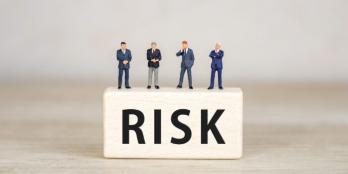RISKと書かれた木のブロックの上にスーツ姿のミニチュア人形が4人立っている