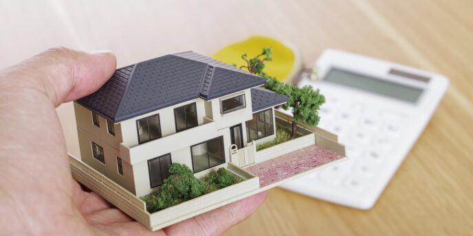 住宅模型を手に持ち、背景に電卓が置かれている画像