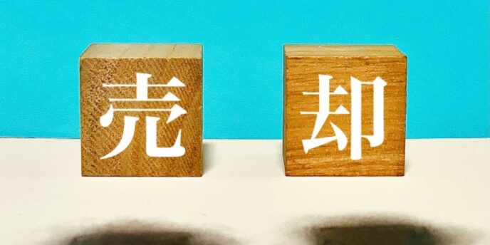 青背景に並ぶ木製ブロックの「売却」文字イメージ
