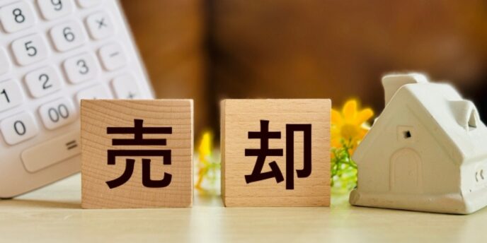 売却に関するイメージ、木製ブロックの「売却」と家型オブジェと電卓が並ぶ