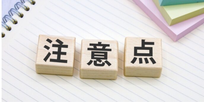 ノートの上に「注意点」と書かれた木製ブロック、確認や警告のイメージ