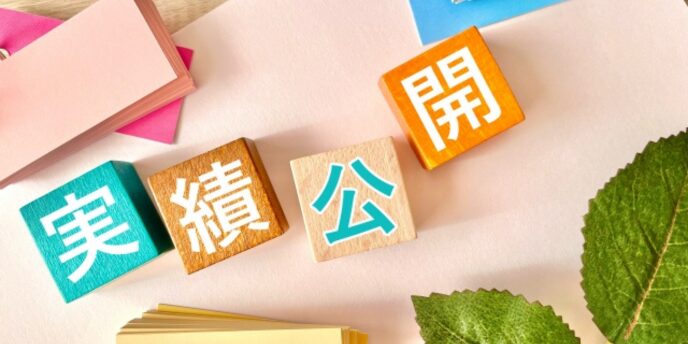 「実績公開」と書かれたカラフルな積み木と、葉やメモ帳などが並ぶ明るい雰囲気の画像。