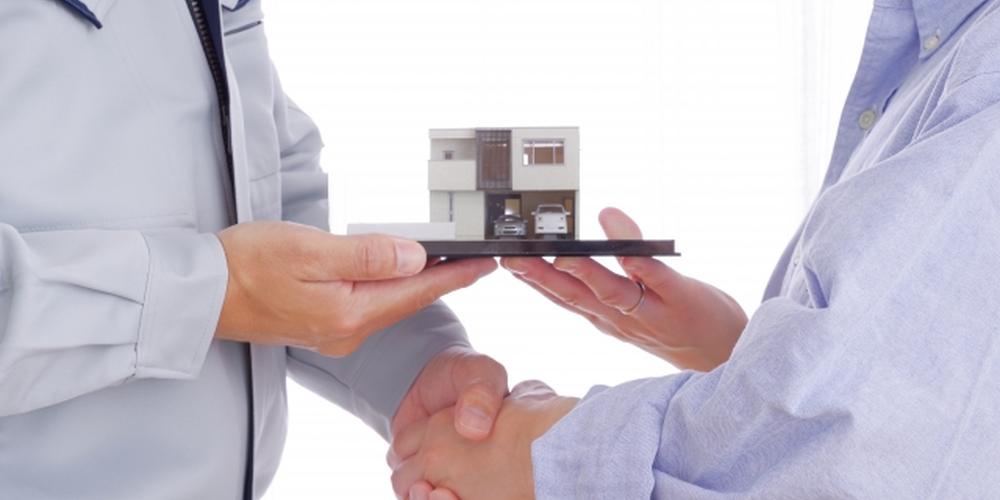 住宅模型を手渡し握手する様子から、不動産契約や信頼関係を表現したイメージ