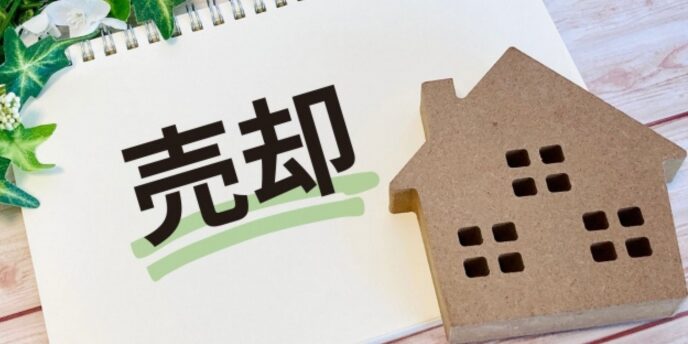 「売却」と書かれたノートと家の模型、不動産売却のイメージ