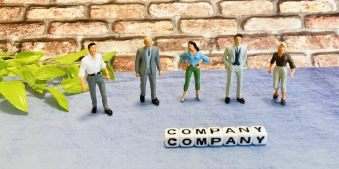 レンガ壁の前に5人のビジネスマンのフィギュアが並び、「COMPANY」と書かれたキューブが置かれている画像