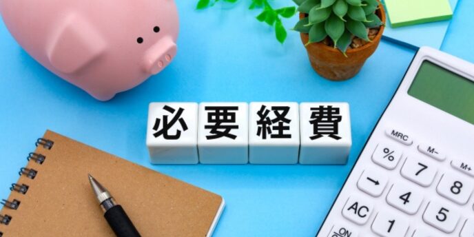 白いブロックに「必要経費」と書かれており、周囲に電卓、ノート、ペン、観葉植物、貯金箱が配置された画像