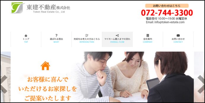 夫婦と担当者が資料を見ながら相談している様子。上部に会社名と連絡先が記載された不動産会社の案内画像