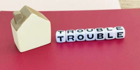 赤い背景の上に「TROUBLE」と書かれたブロックと家の模型が置かれている画像