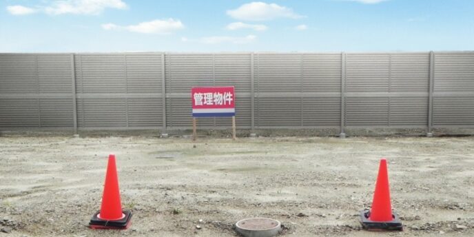 更地に立つ「管理物件」の看板と赤いパイロン