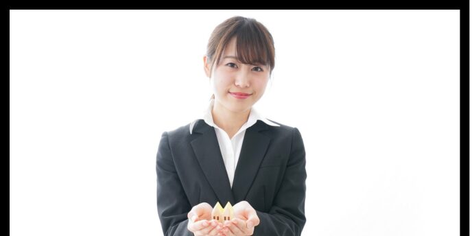 家の模型を両手で持つスーツ姿の女性の画像(背景は白)