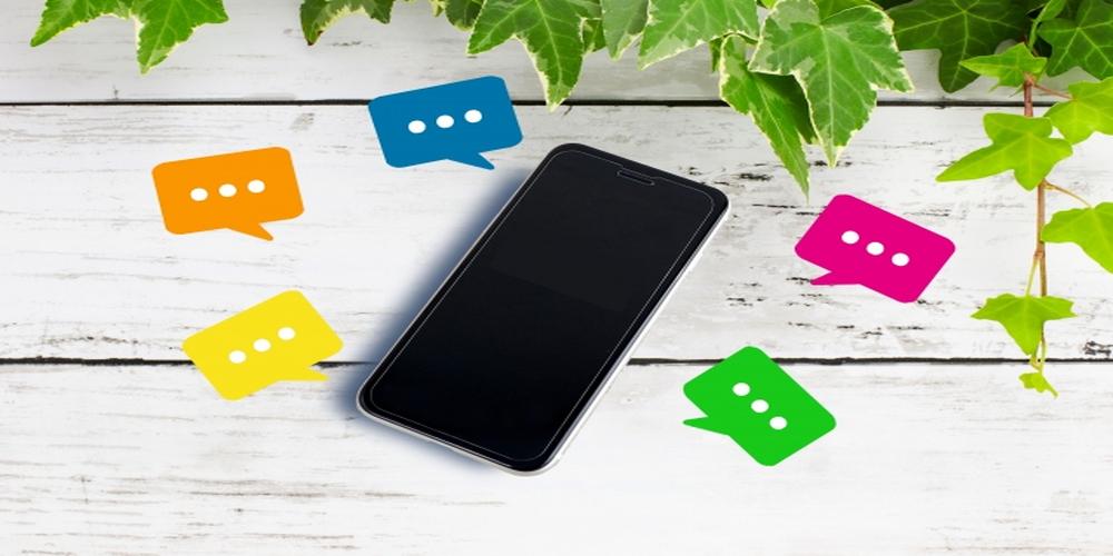 スマートフォンの周りにカラフルな吹き出しアイコンが浮かぶ木目背景のイメージ
