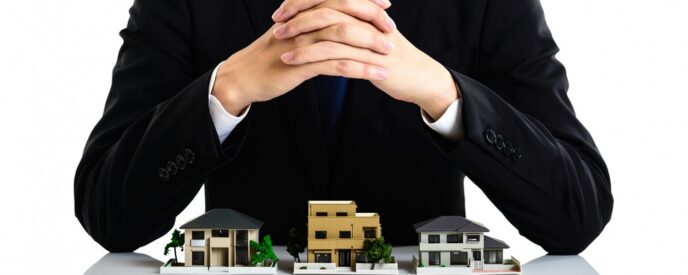 不動産ミニチュア模型の前で手を組むスーツ姿の男性