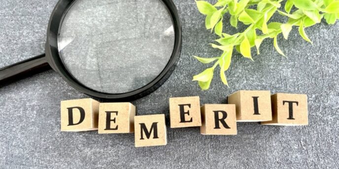 黒い背景に「DEMERIT」と書かれた積み木と虫眼鏡、緑の葉が添えられた画像