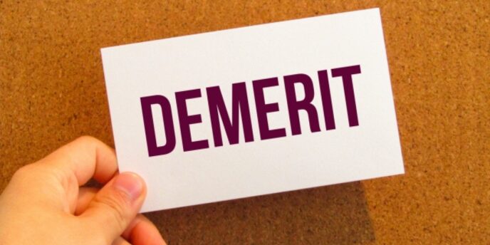 「DEMERIT」と書かれたカードを手で持っている画像。背景はコルクボード。