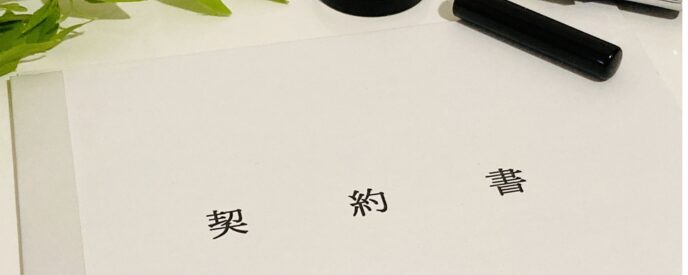「契約書」と書かれた書類と黒いペンが並ぶ画像