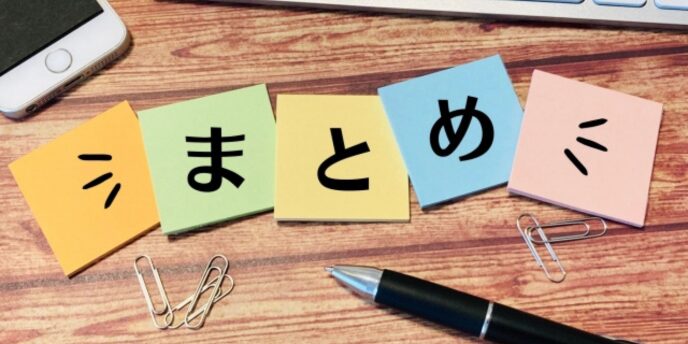 カラフルな付箋に「まとめ」と書かれた文字が並び、ペンやクリップが周囲に置かれたデスクの画像。