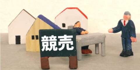 「競売」と書かれた看板とミニチュアの家と人物