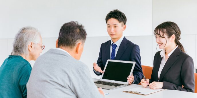 若い男女2人のファイナンシャルプランナーがシニア夫婦に説明している場面