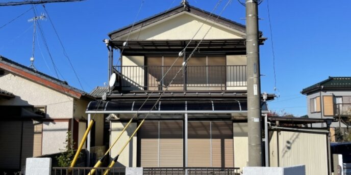 住宅街に建つ和風の二階建て一軒家、青空のもと電柱と電線が目立つ外観